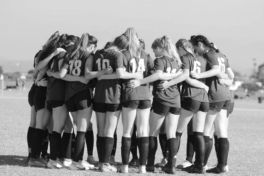 A Los Angeles Sports Club team stands in a huddle on the field, arms around each other's shoulders.